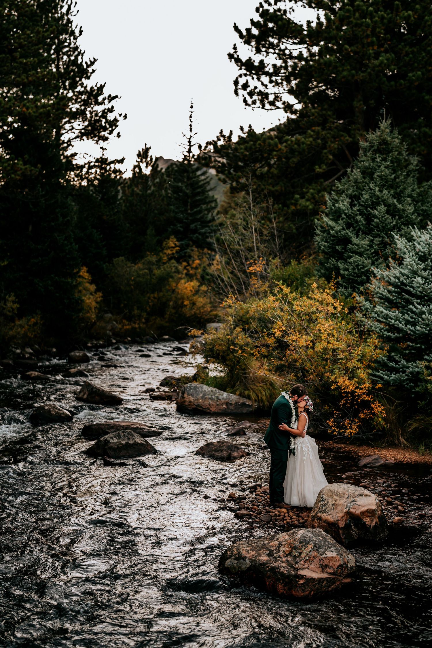 A scenic mountain path with rocky terrain and autumn foliage creates a dramatic backdrop for a wedding photoshoot.