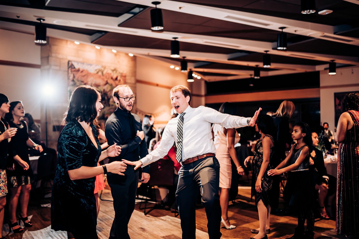 Wedding guests dancing energetically on the dance floor at an indoor reception.