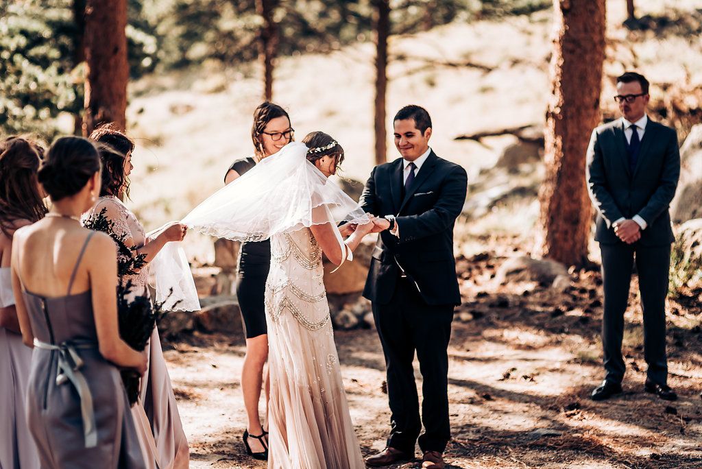 A wedding ceremony moment captured in a pine forest with soft natural lighting filtering through the trees.