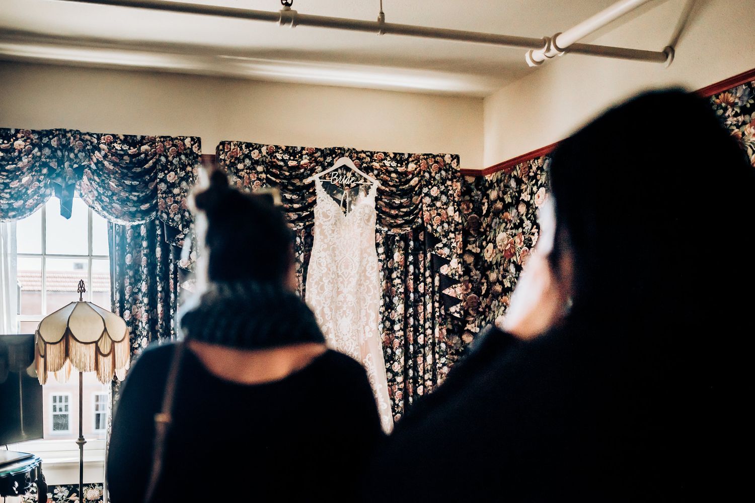 Wedding dress hanging from ceiling with decorative lights and floral arrangements.