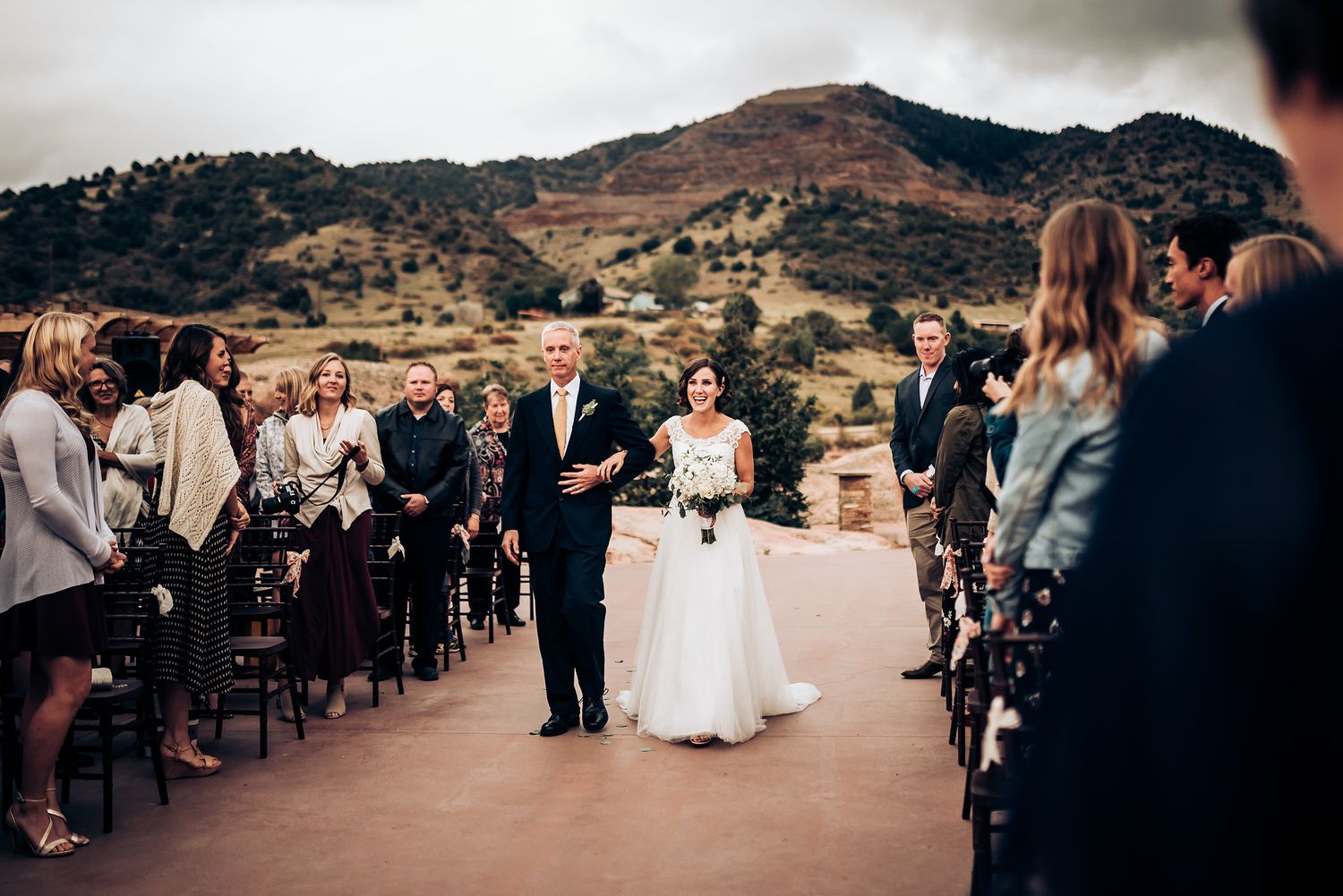 An outdoor wedding ceremony takes place with mountains in the background.