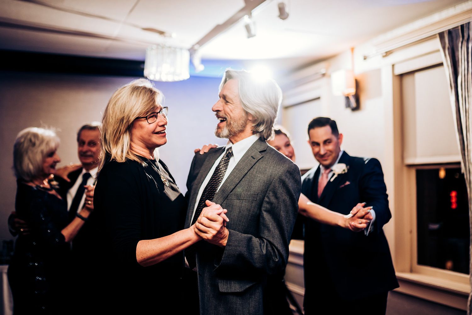 Couples dancing at an elegant indoor reception with ambient lighting.