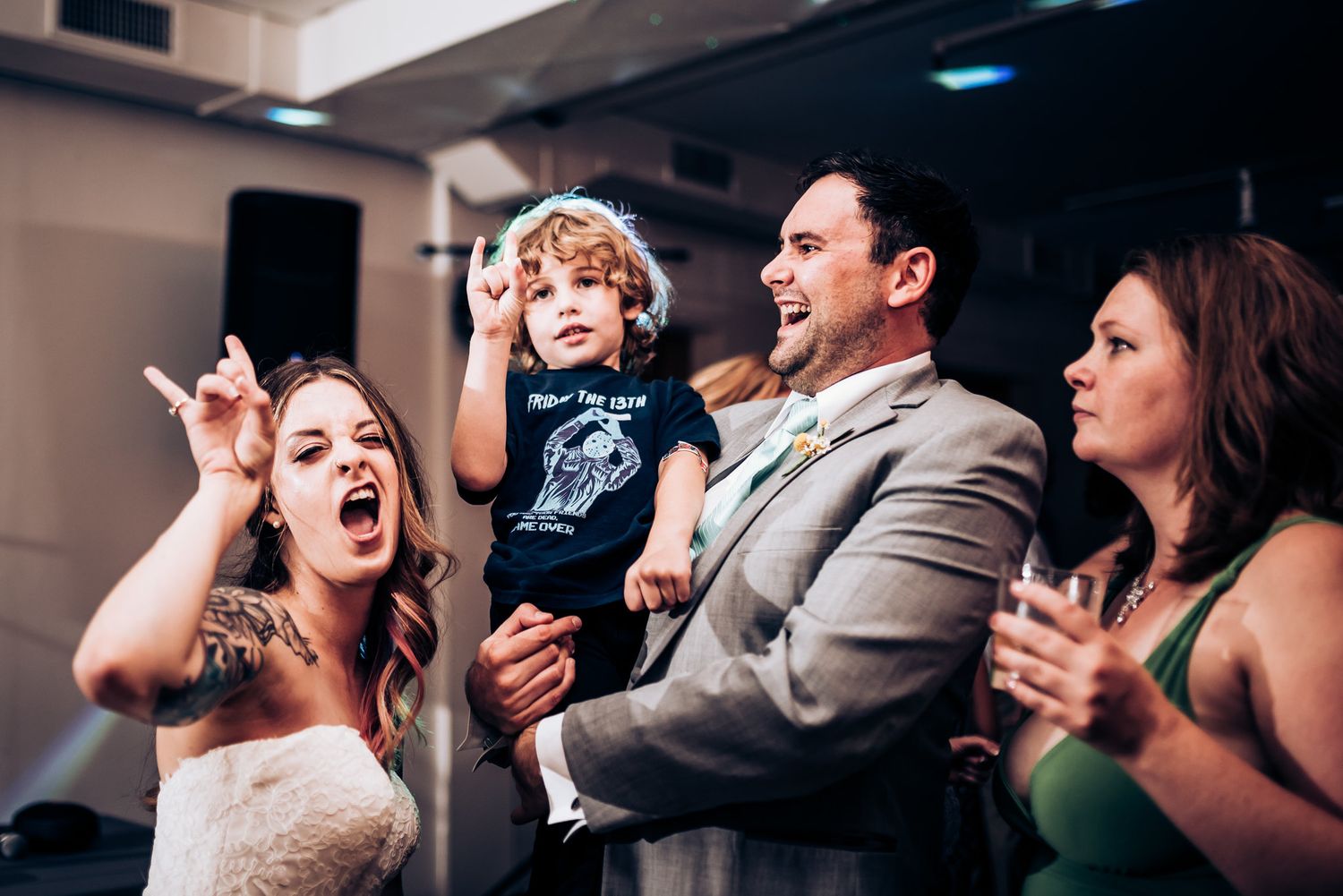Wedding party celebrates energetically during reception under indoor venue lighting.