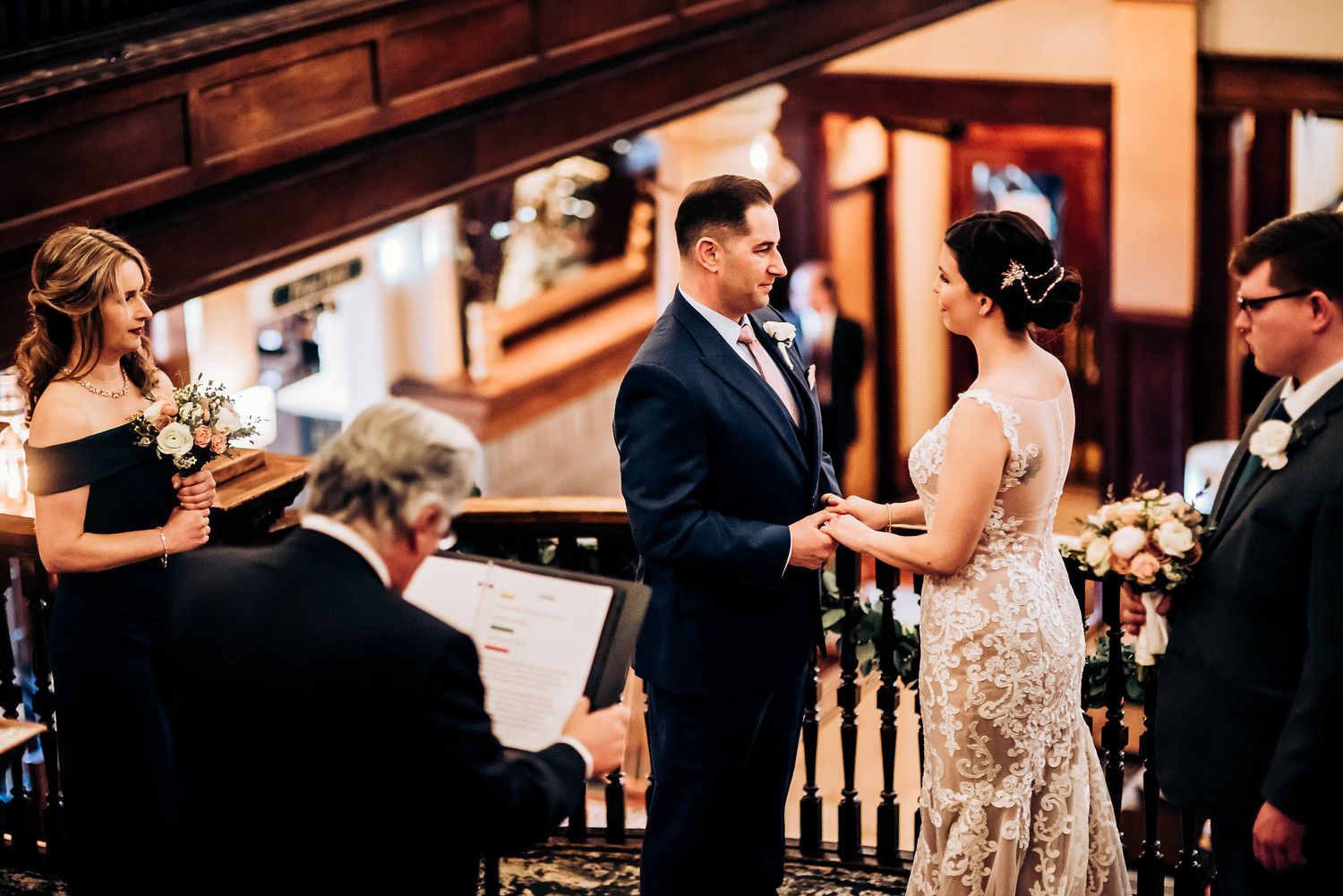 Exchange of rings during wedding ceremony on wooden staircase landing with warm lighting.