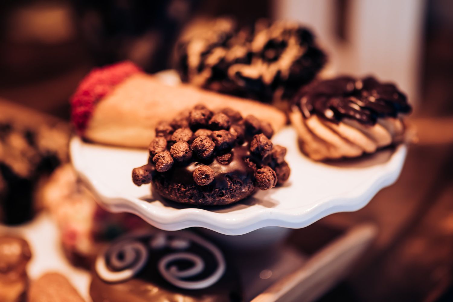 Close-up of chocolate covered donuts and pastries on white cake stand.