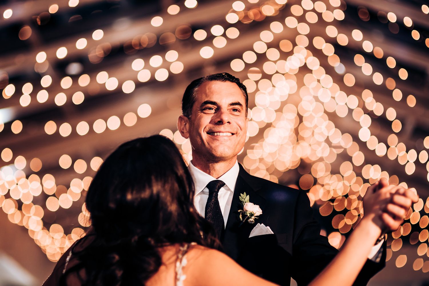 Wedding dance captured under warm glowing fairy lights at indoor reception.
