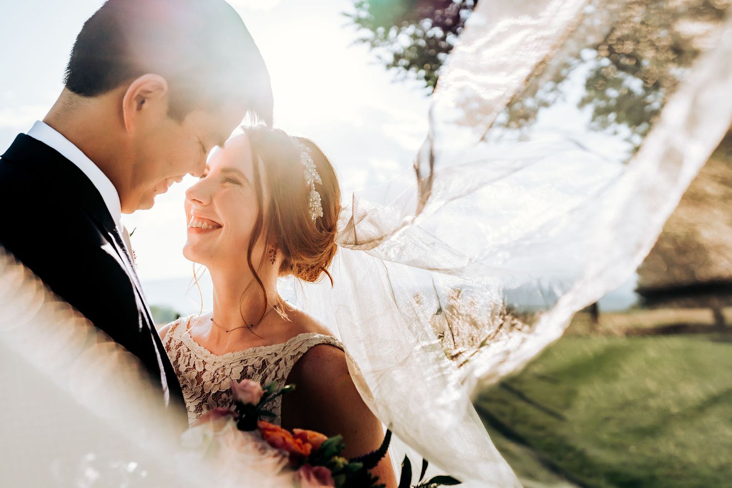 Ethereal wedding portrait with flowing veil catching sunlight in an outdoor setting.