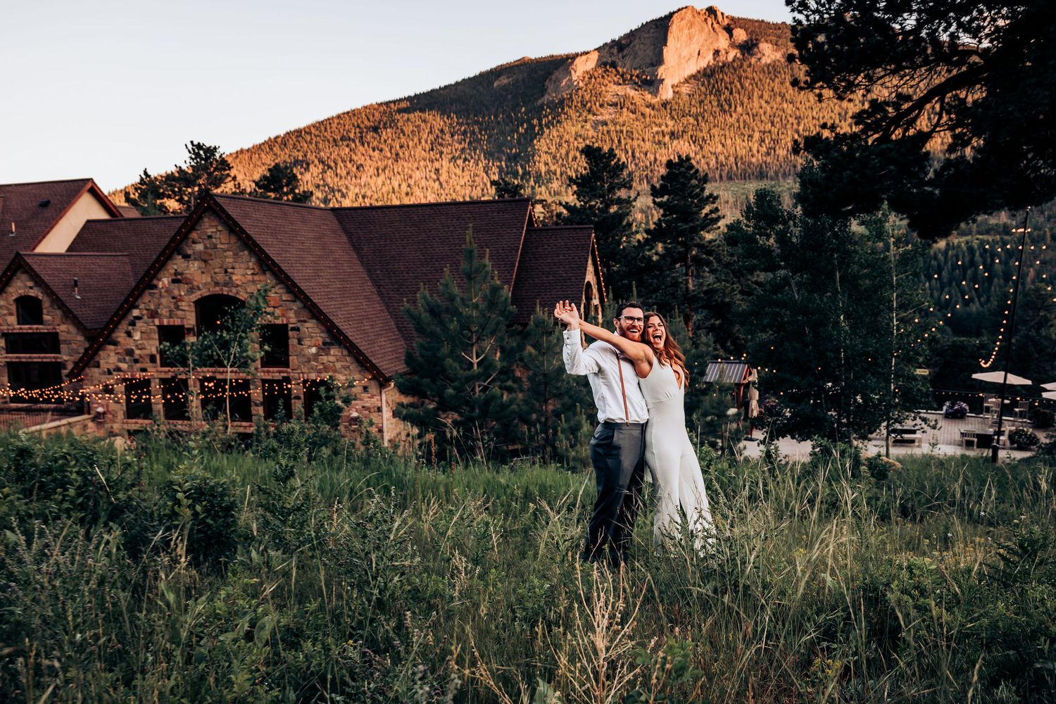 Dancing couple silhouetted against sunset with rustic lodge and mountains in background.
