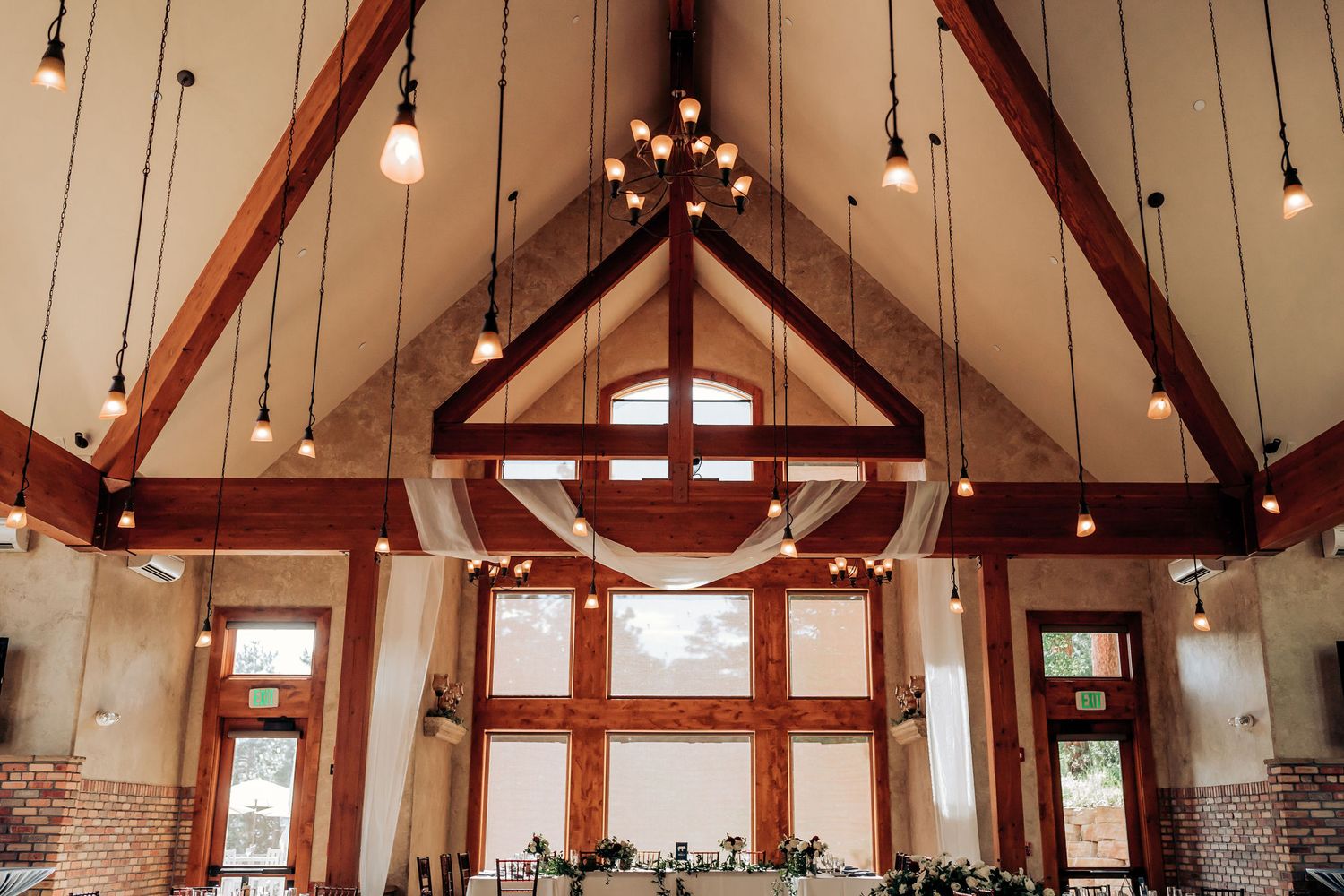Cathedral ceiling wedding venue with exposed wooden beams and pendant lighting.
