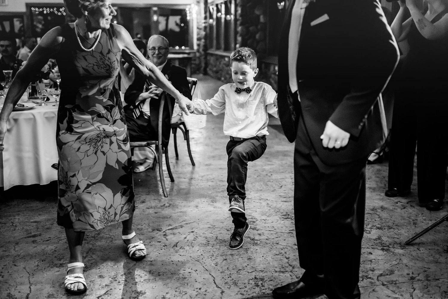 A young boy dances energetically on the reception dance floor while guests watch and smile.