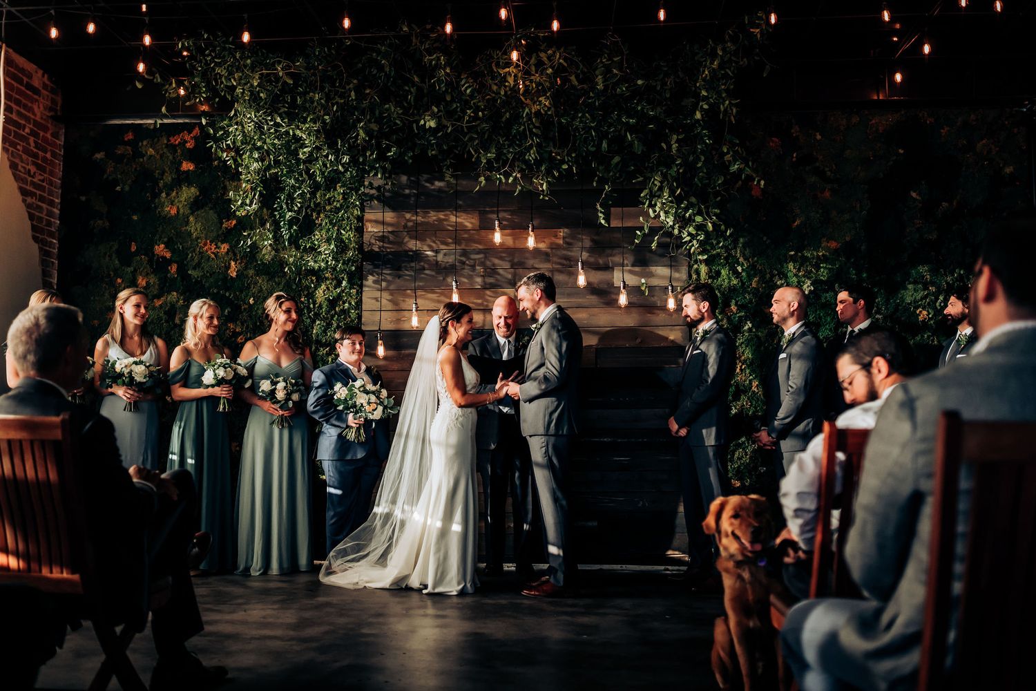 Wedding ceremony in industrial venue with string lights and greenery decorations.