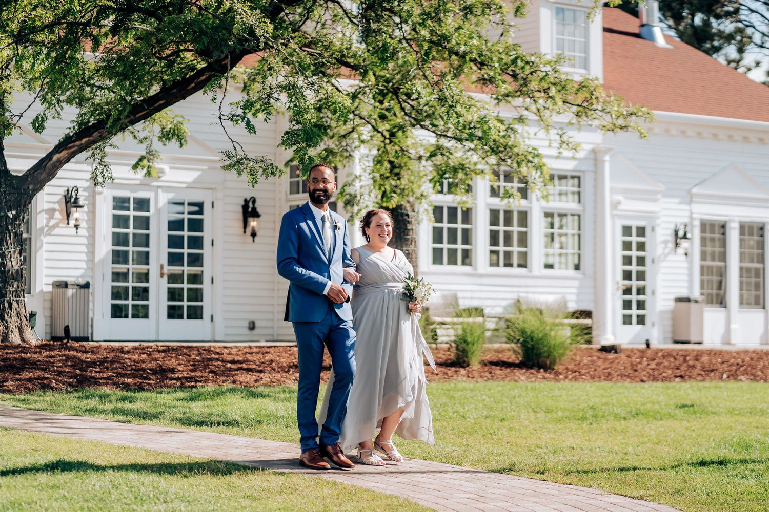 Couple in formal attire posing outside classic white colonial style building.