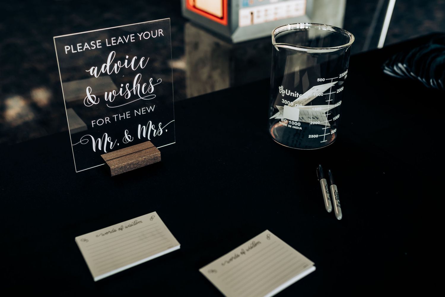 A guest book station with advice cards and a decorative glass cup on a dark table surface.