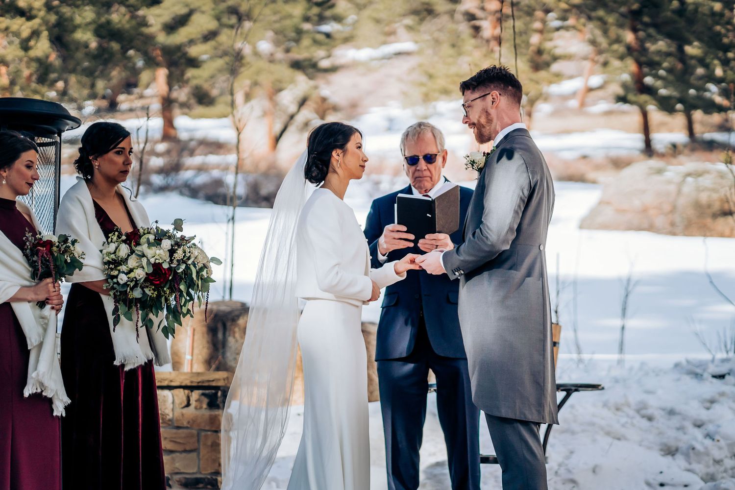 Winter wedding ceremony exchange with officiant under wooden pavilion.