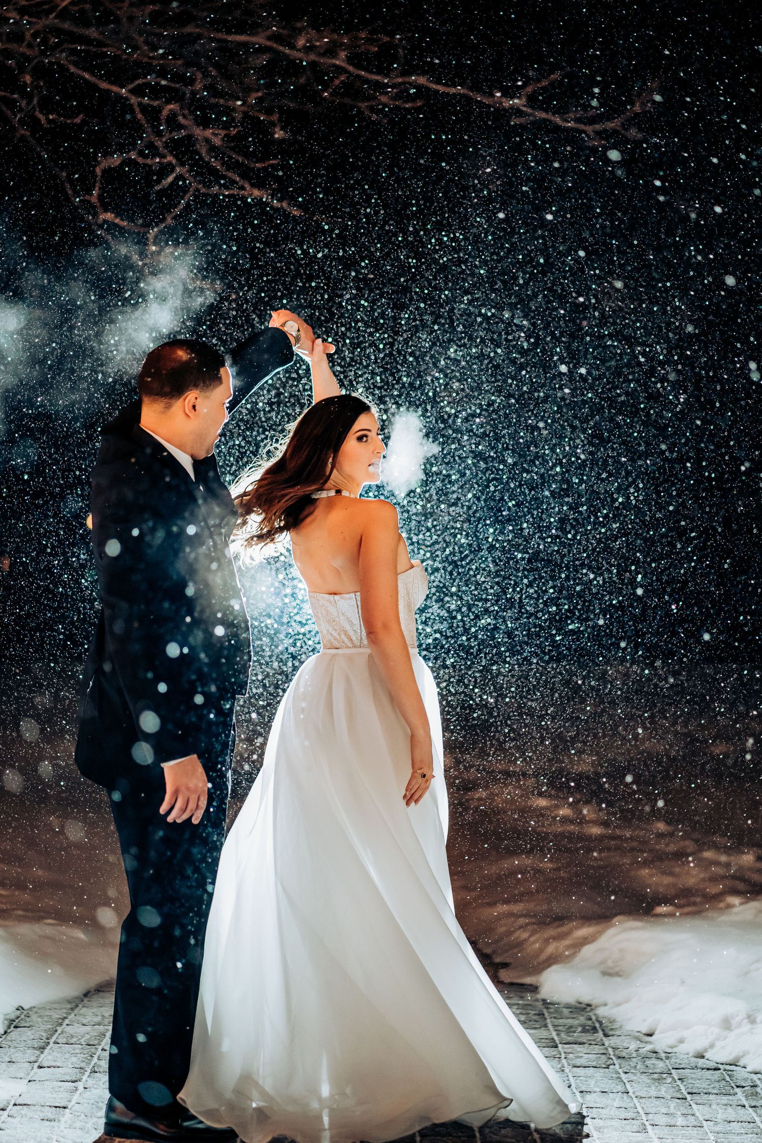 Enchanting winter wedding dance portrait with snow falling and twinkle lights in background.