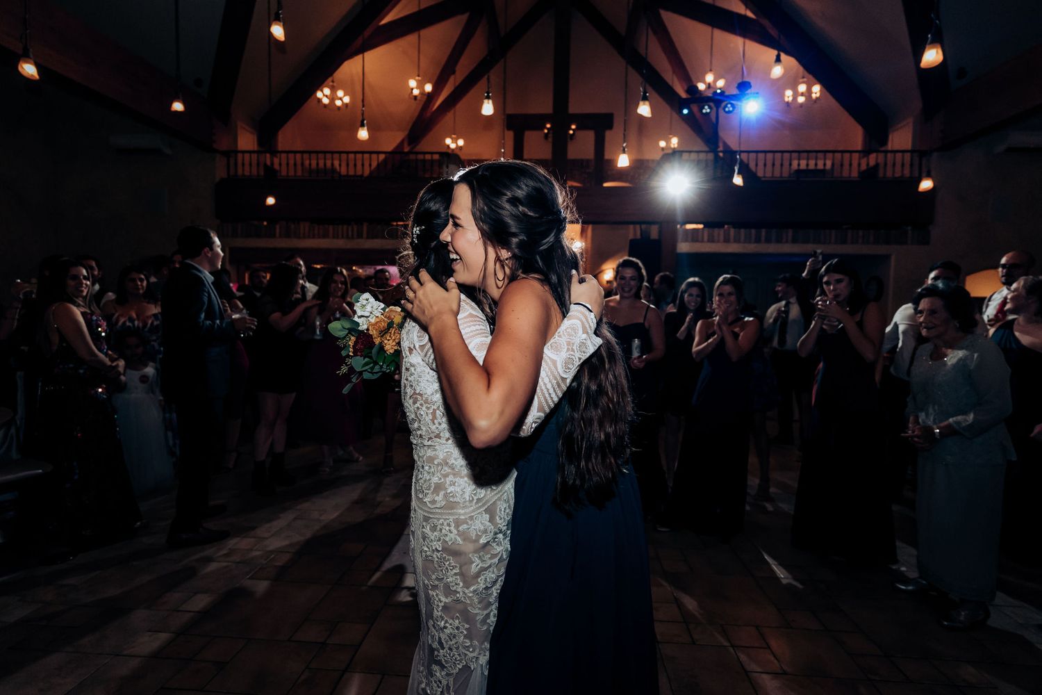 Couples dance together at an evening wedding reception in a rustic venue with exposed wooden beams and string lights.
