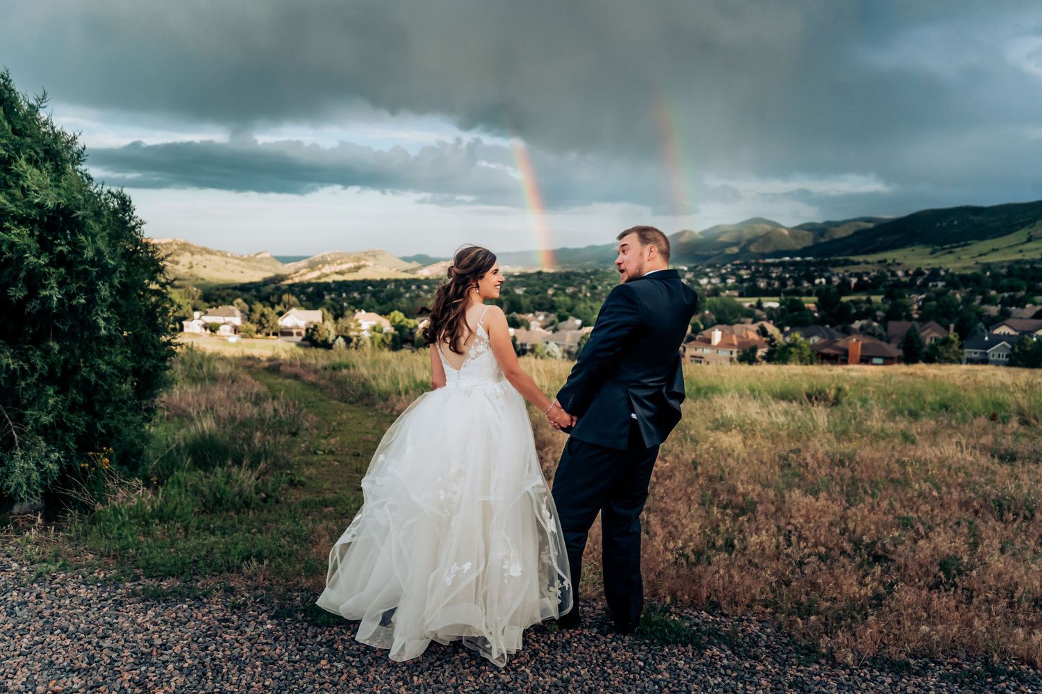 Newlyweds enjoy a scenic mountain view with a rainbow stretching across the stormy sky.
