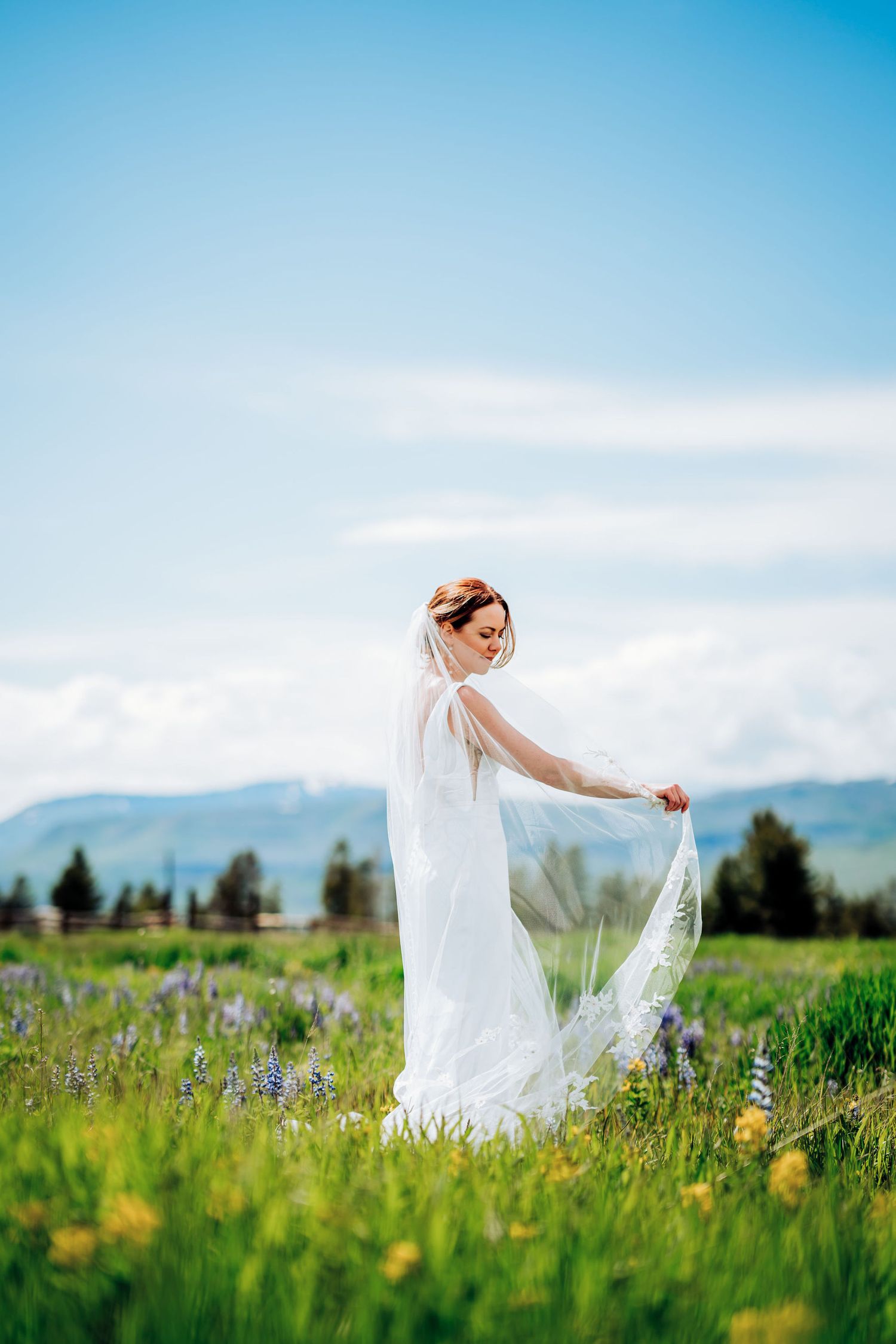 A bride in white dress twirls in a mountain meadow filled with wildflowers.