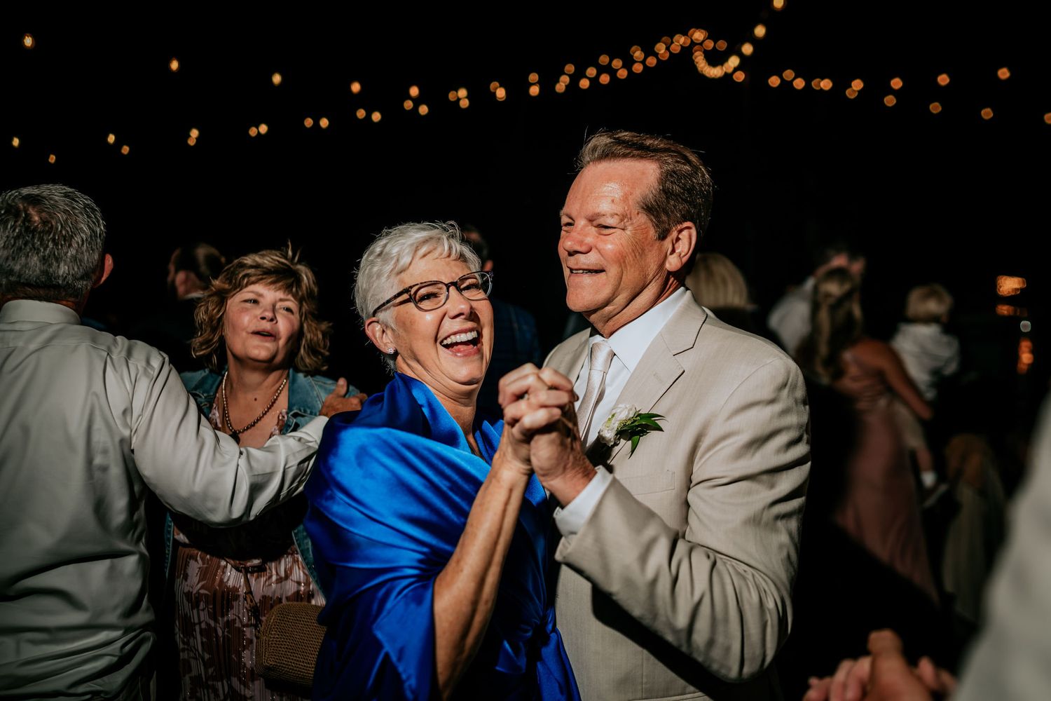 Wedding guests dancing and celebrating under warm lighting at an evening reception.