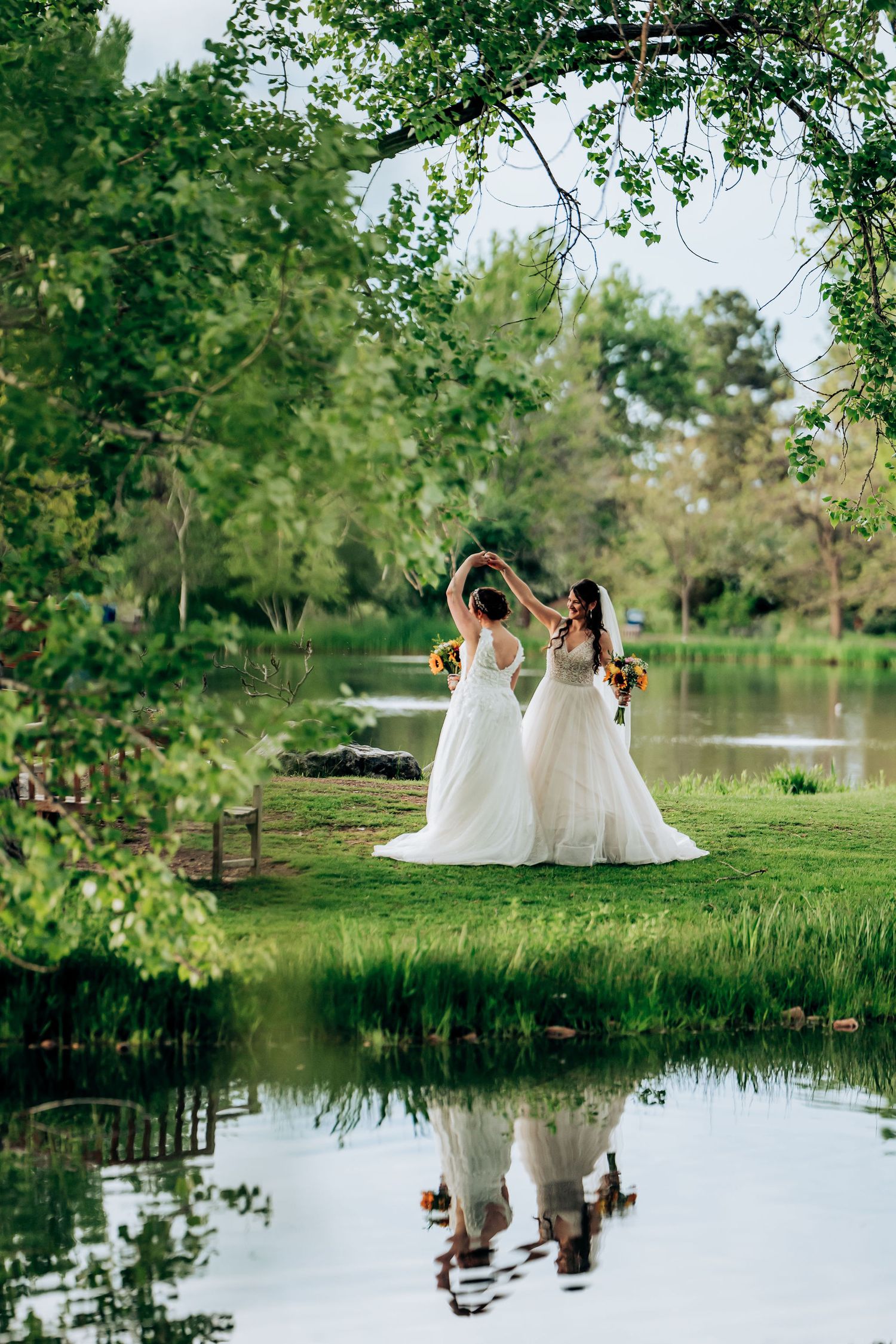 Two figures in white dresses standing by reflective pond with their reflection visible in water.