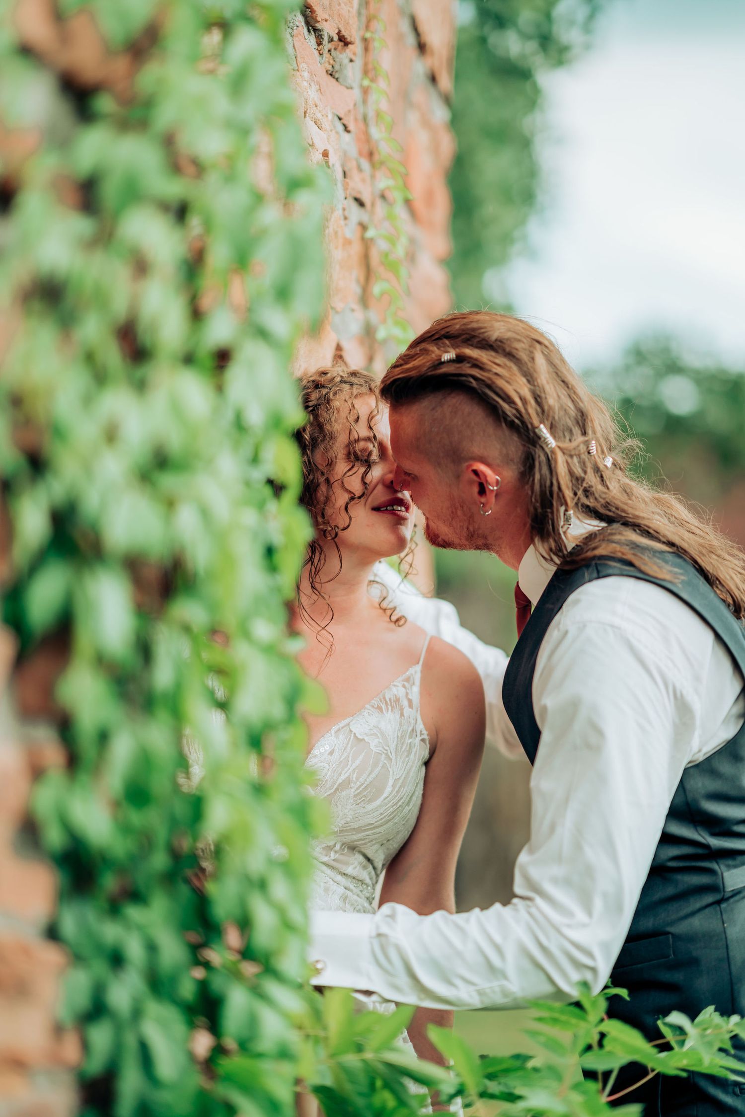 A romantic moment captured between newlyweds against a vine-covered brick wall.