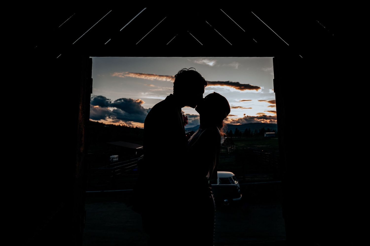 Dark silhouettes of two people in intimate moment with vibrant sunset backdrop.