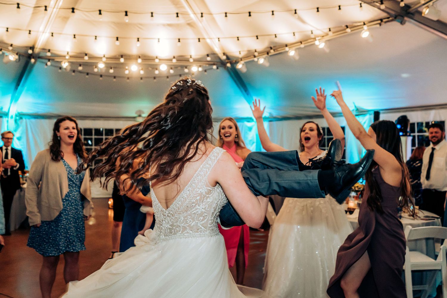 Wedding guests dancing joyfully under twinkling lights at indoor reception venue.