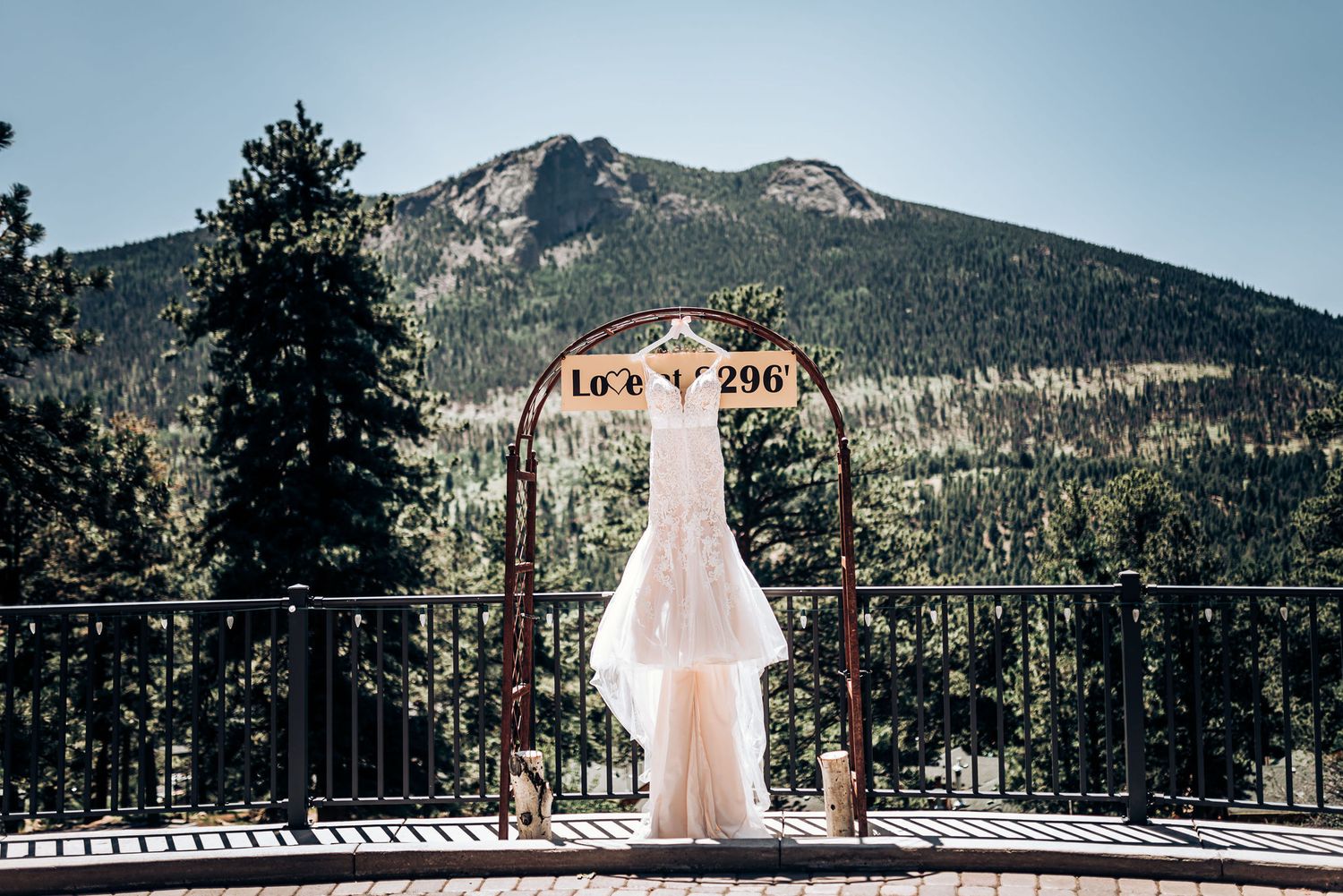 A white wedding dress displayed on an arch against a scenic mountain landscape backdrop.
