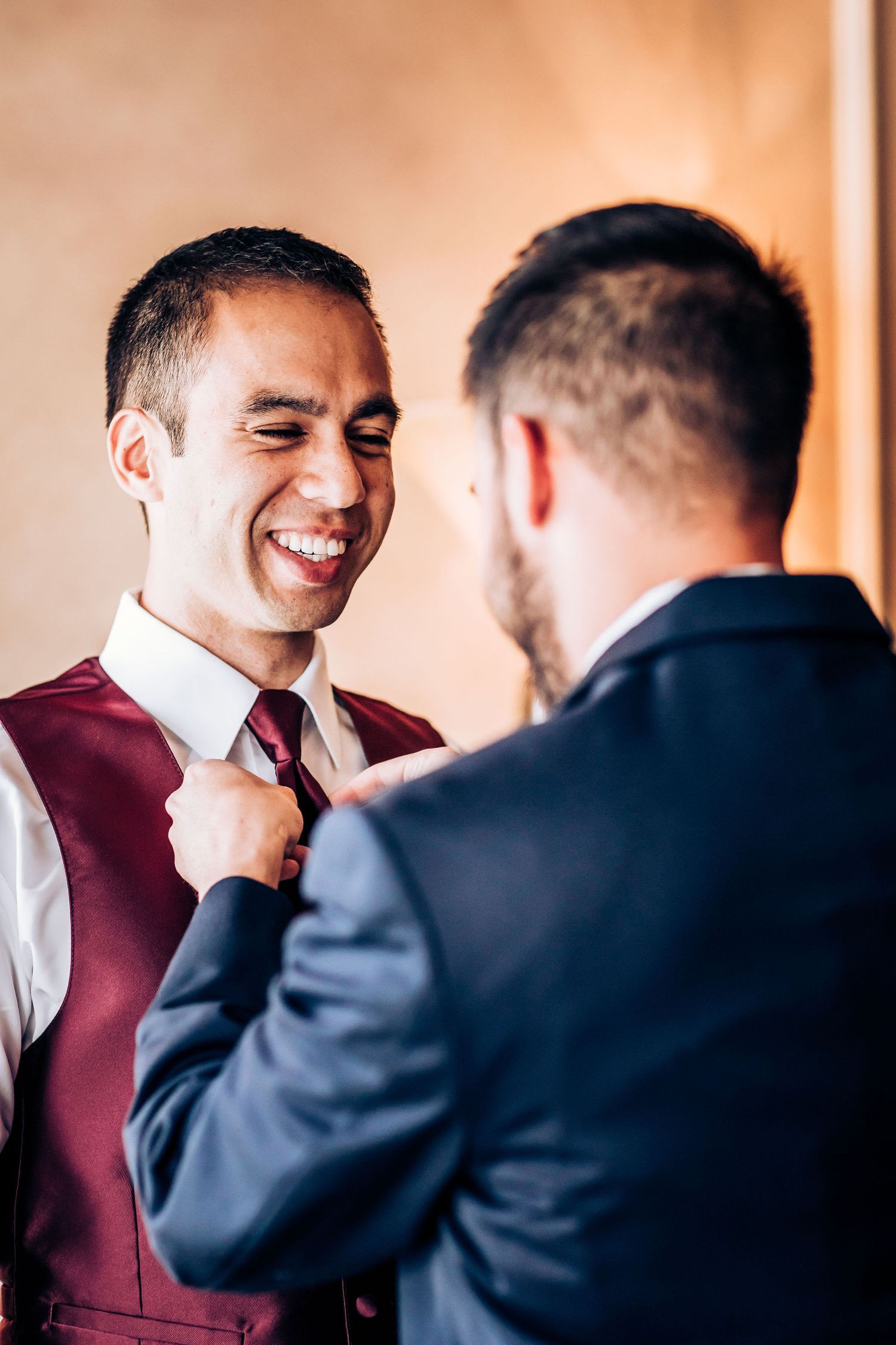 Two men share a joyful moment while adjusting formal attire.