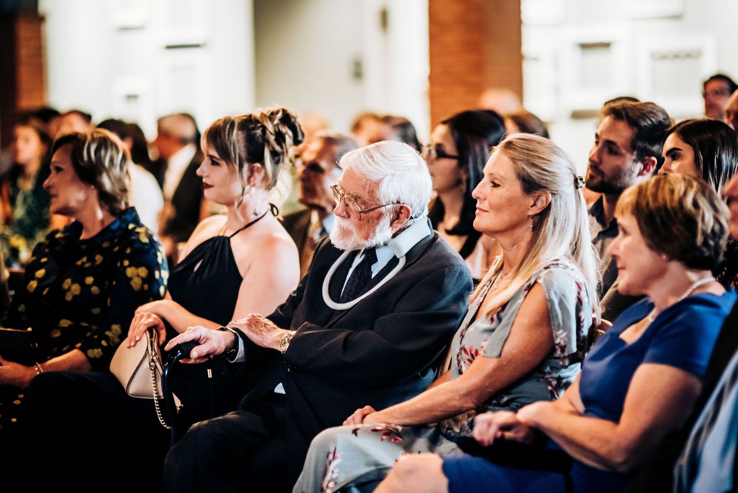 Wedding guests seated in rows watching ceremony in elegant indoor venue.