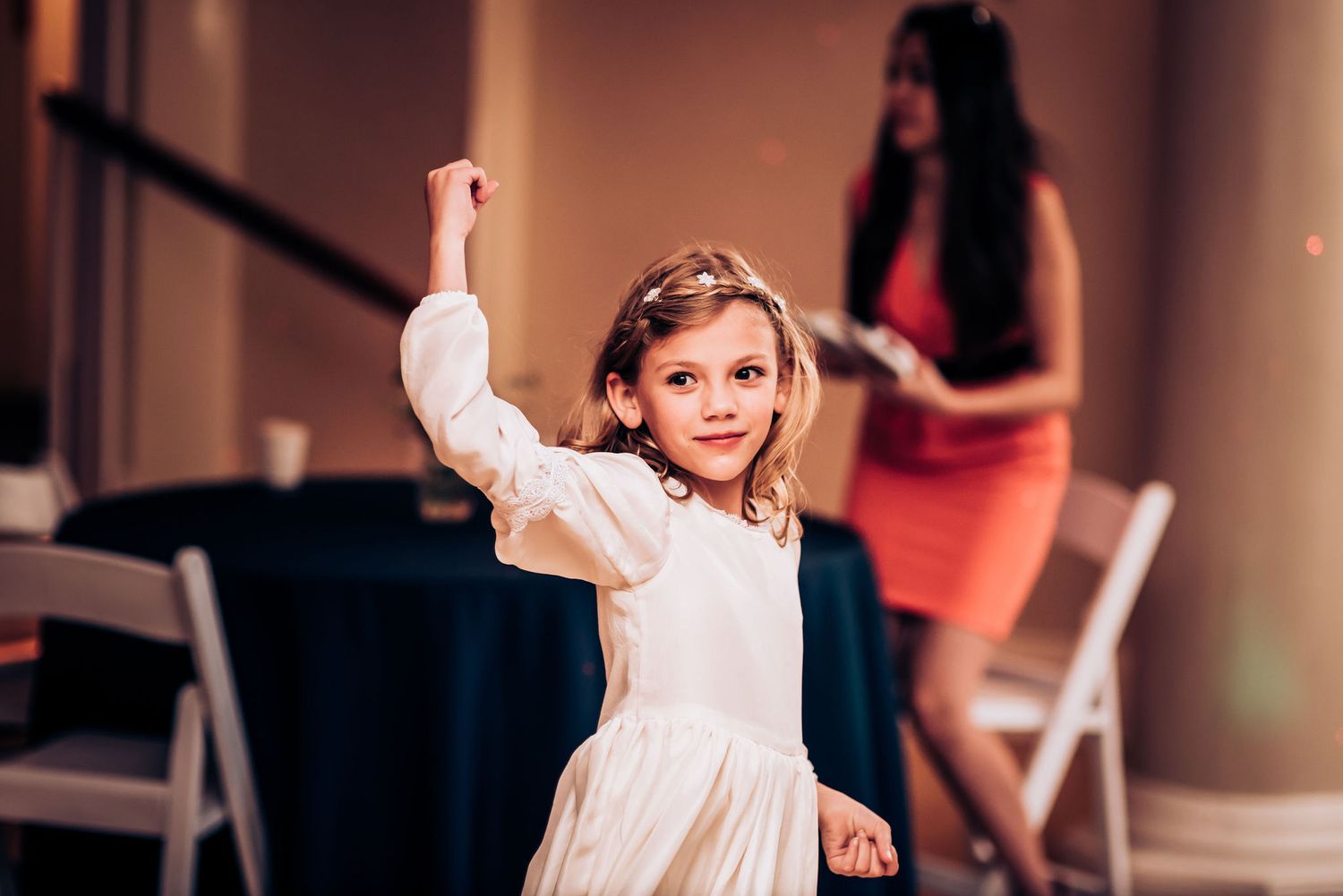 A young dancer in a white dress performs with enthusiasm during a celebration.