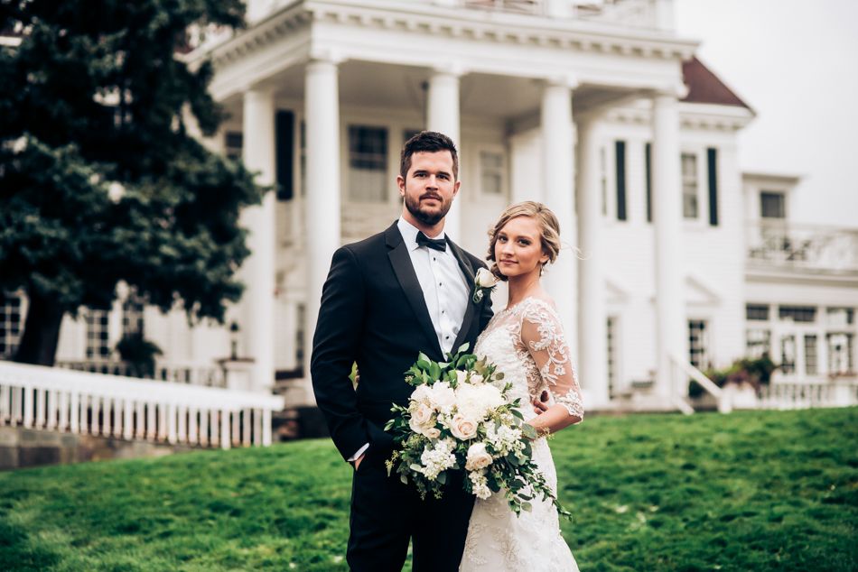 Elegant wedding portrait in front of a classic white mansion with columns and grand architecture.
