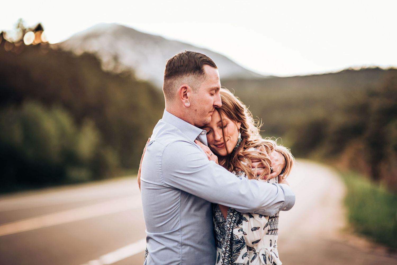 A tender embrace captured during a romantic mountain road photoshoot at dusk.