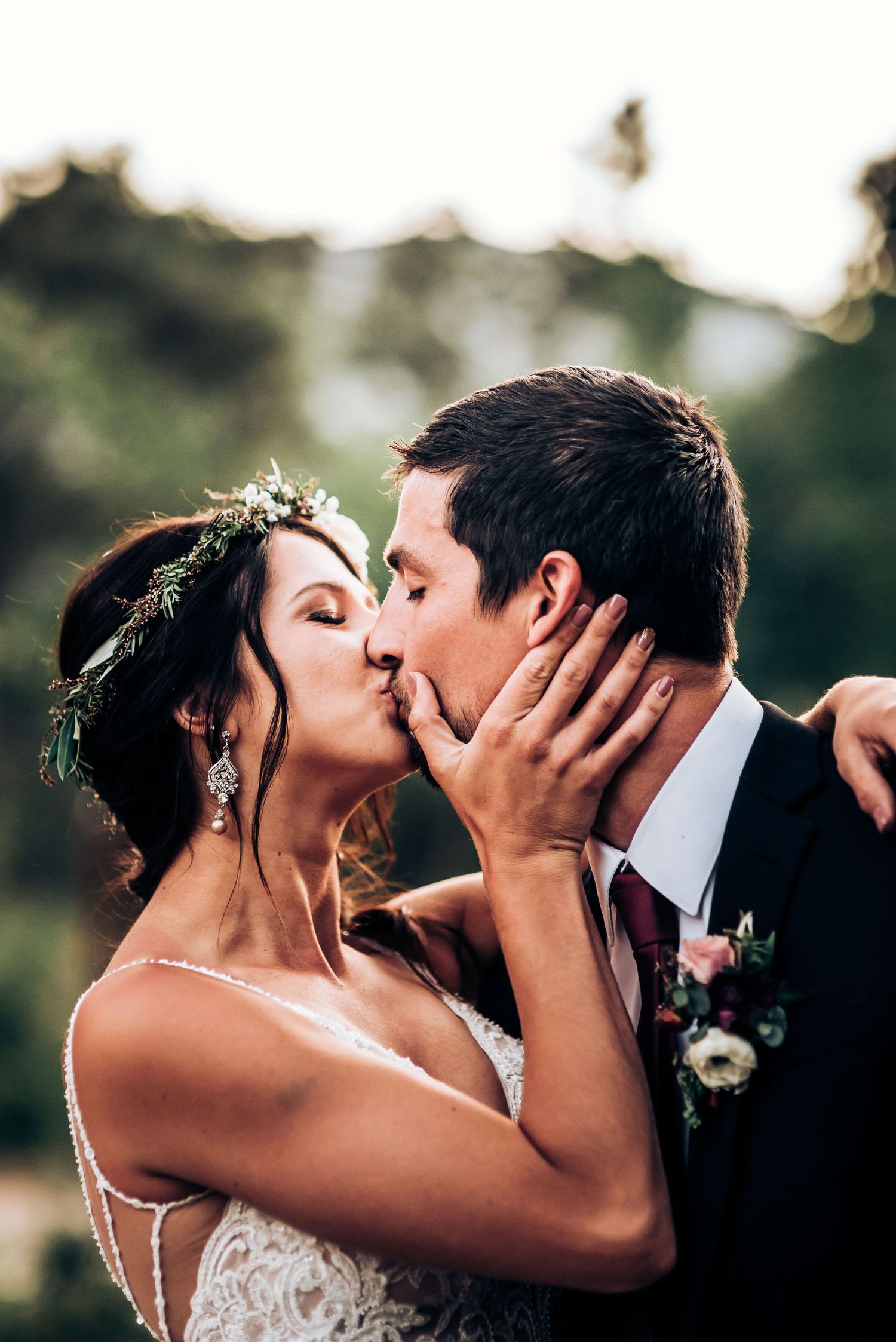 Intimate wedding kiss captured in natural lighting with bride wearing delicate floral crown.