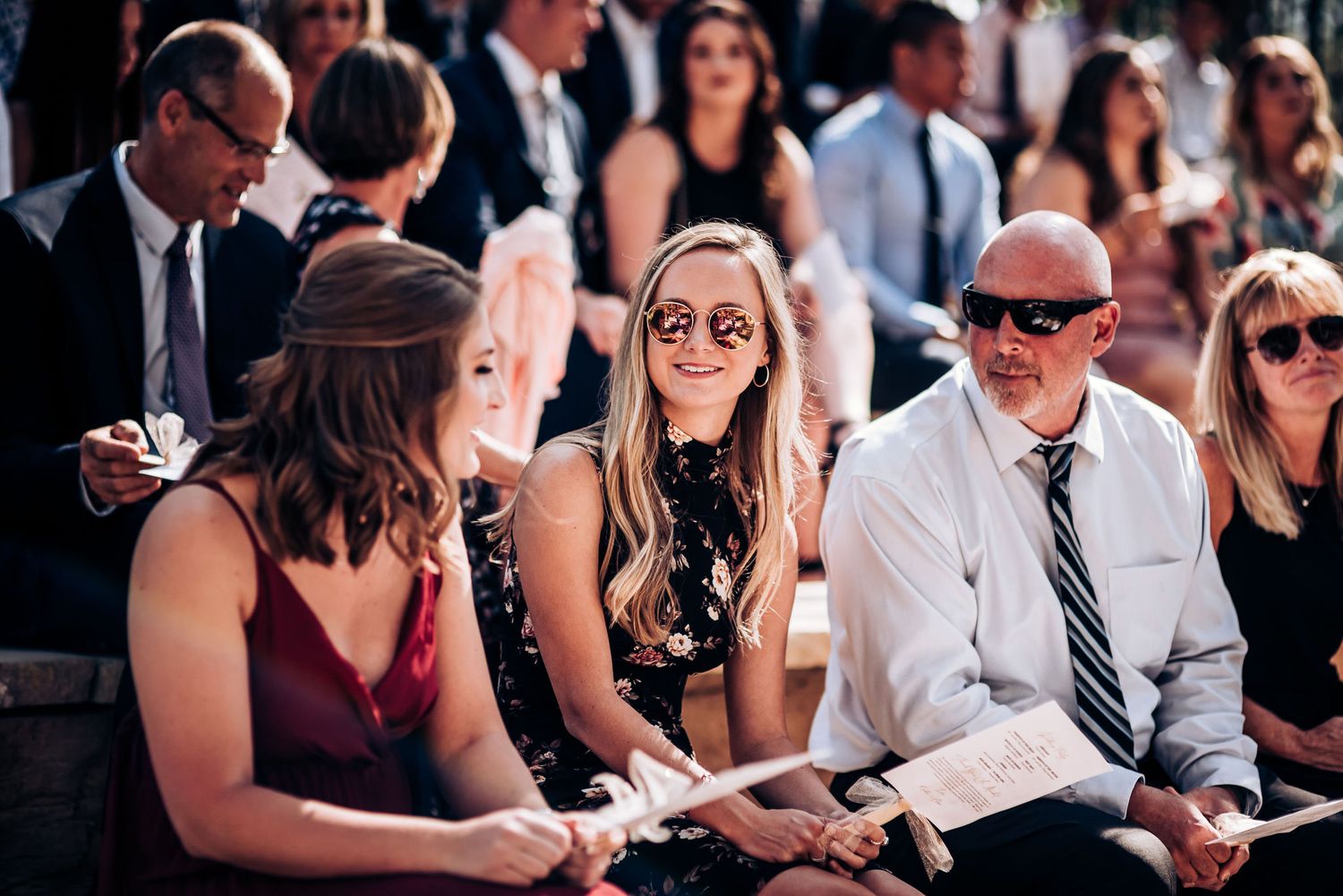 Wedding guests seated outdoors enjoying the ceremony in casual summer attire.