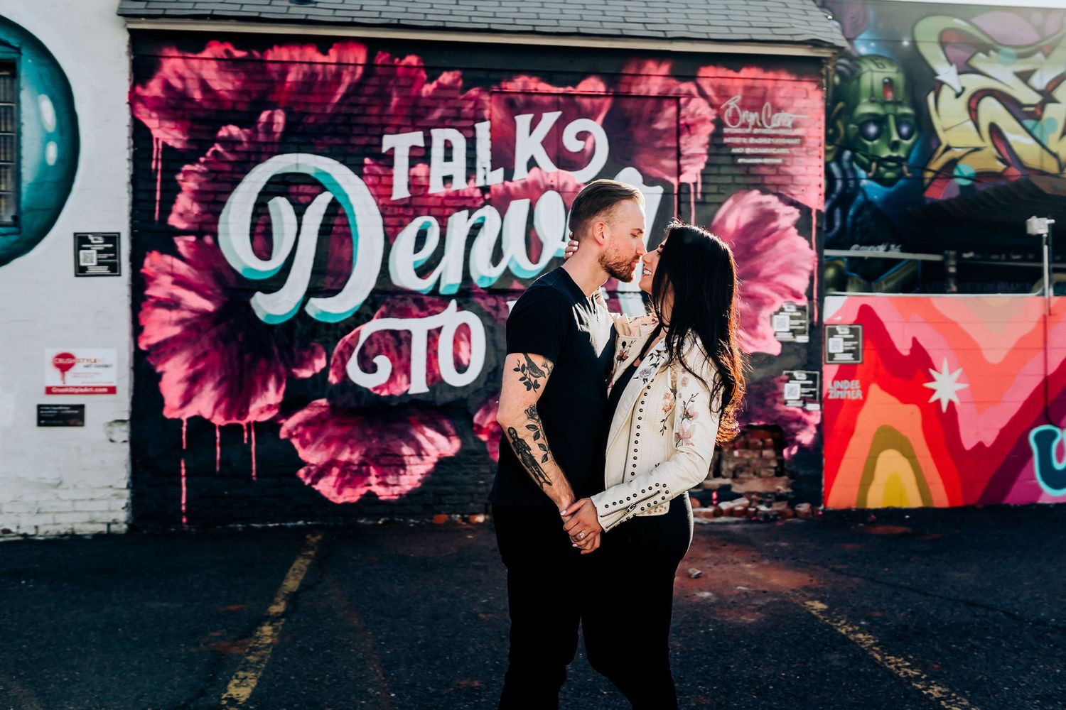 Couple stands in front of vibrant pink floral graffiti mural with stylized text.