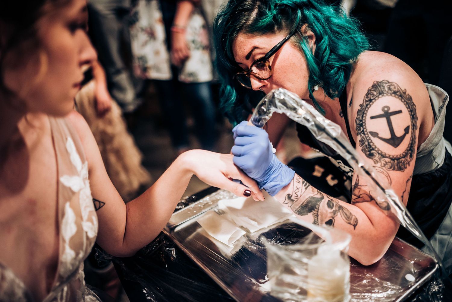 Artist with teal hair and tattoos works on a delicate design at a wedding event.