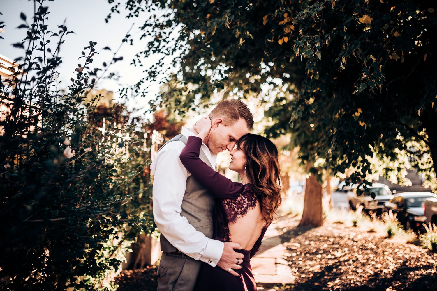 A romantic couple embraces outdoors among autumn trees and dappled sunlight.
