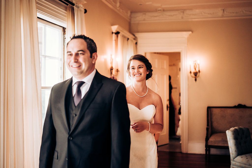 A couple prepares for their first look in an elegant hallway with wall sconces.