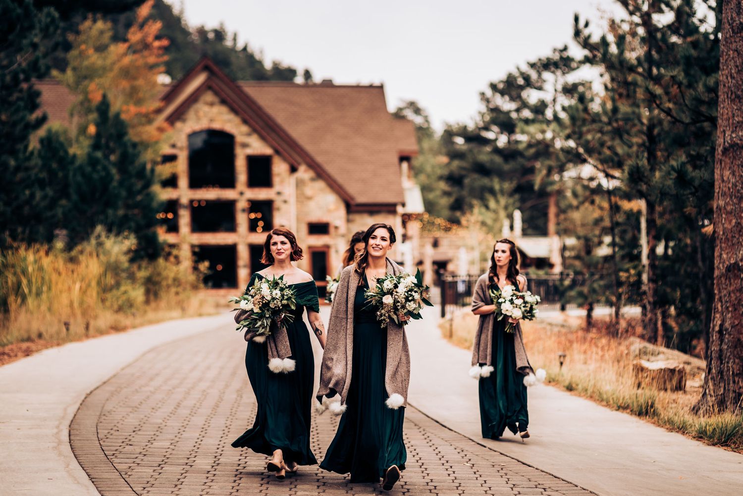 Wedding party members walking along curved path near rustic mountain lodge.