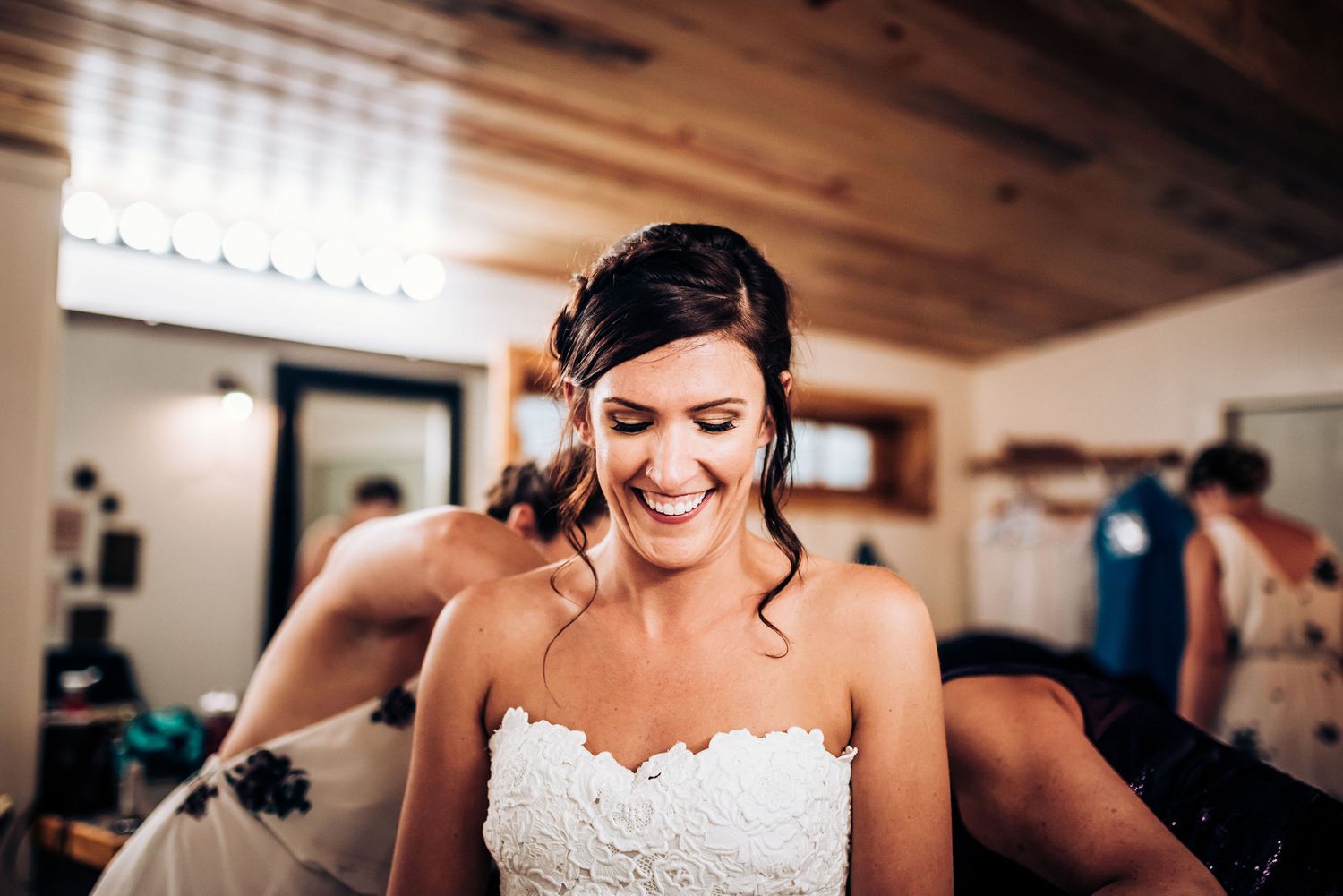 Bride in white lace dress laughing joyfully during wedding preparations.
