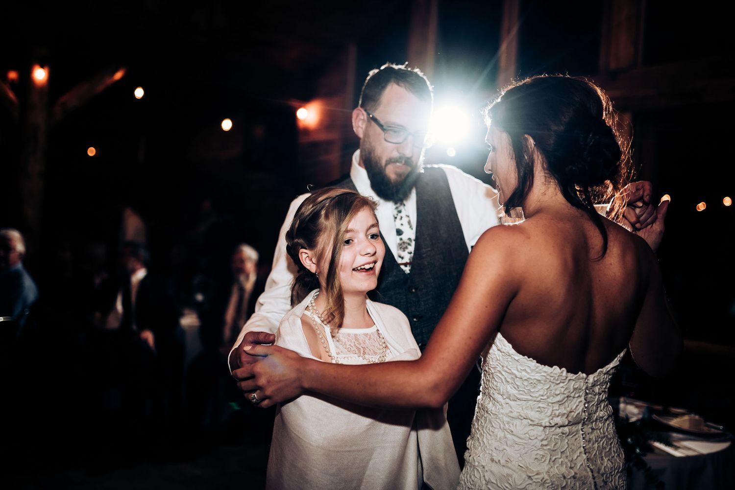A heartwarming dance moment captured at a wedding reception with dramatic backlighting.