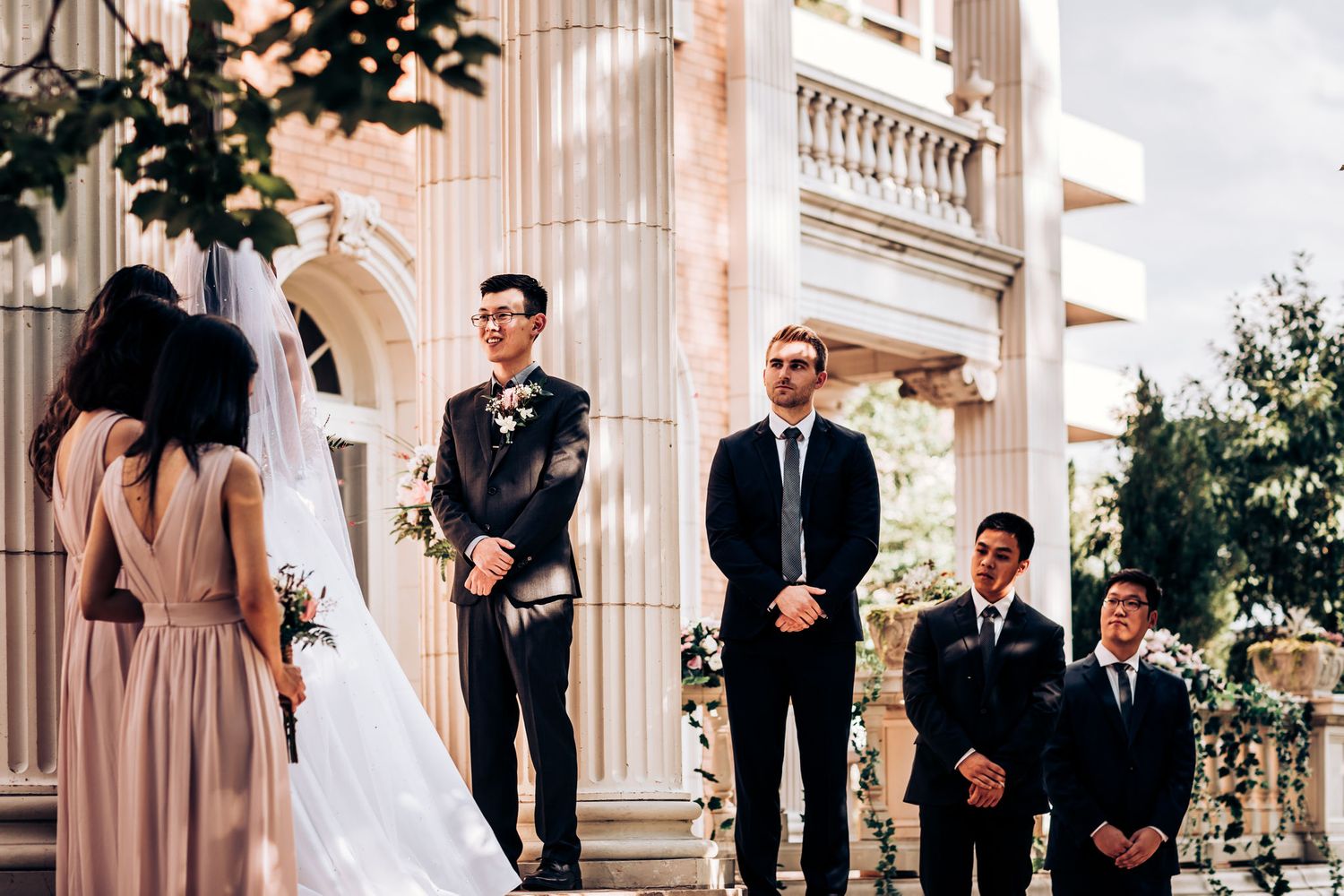 Wedding party stands arranged on historic stone steps during outdoor ceremony.