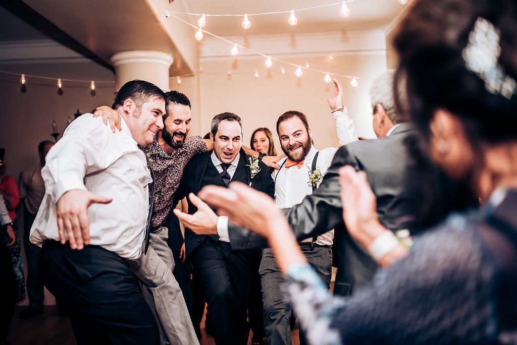 Group of party guests celebrate and pose together under string lights at an indoor reception.