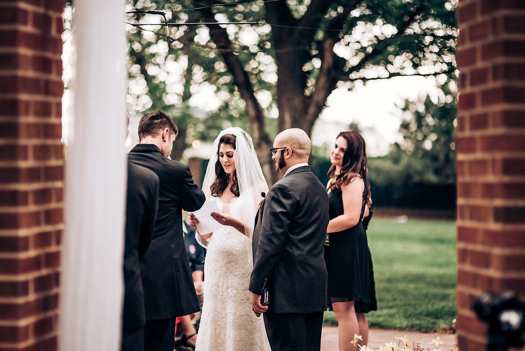 Intimate outdoor wedding ceremony between brick columns with guests watching.