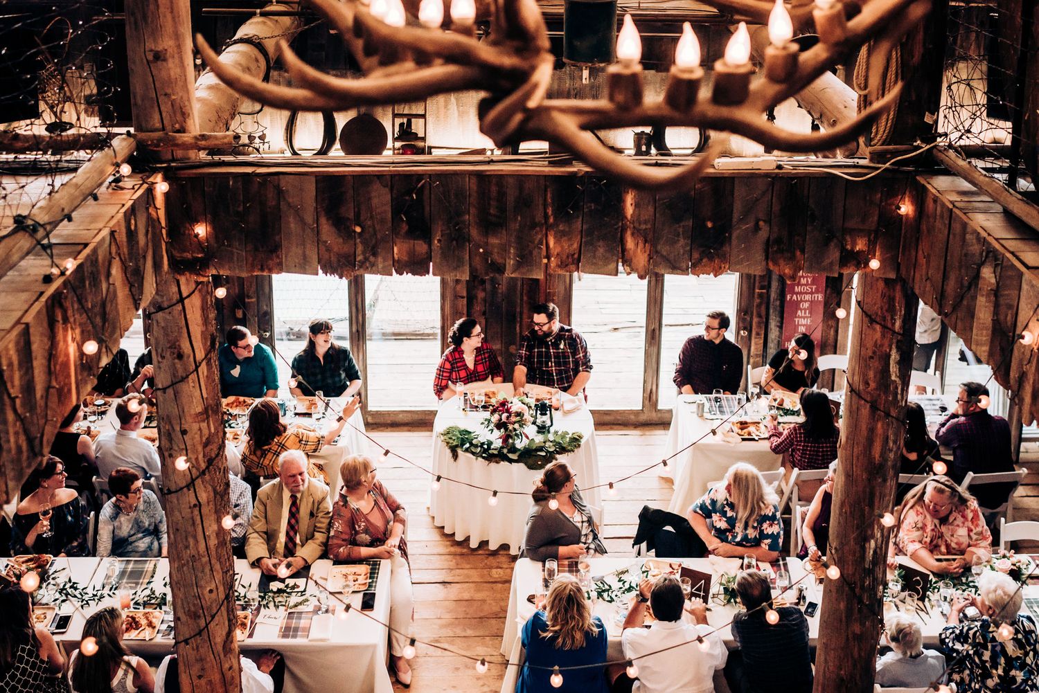 Rustic barn wedding reception with hanging lights and tiered cake centerpiece.