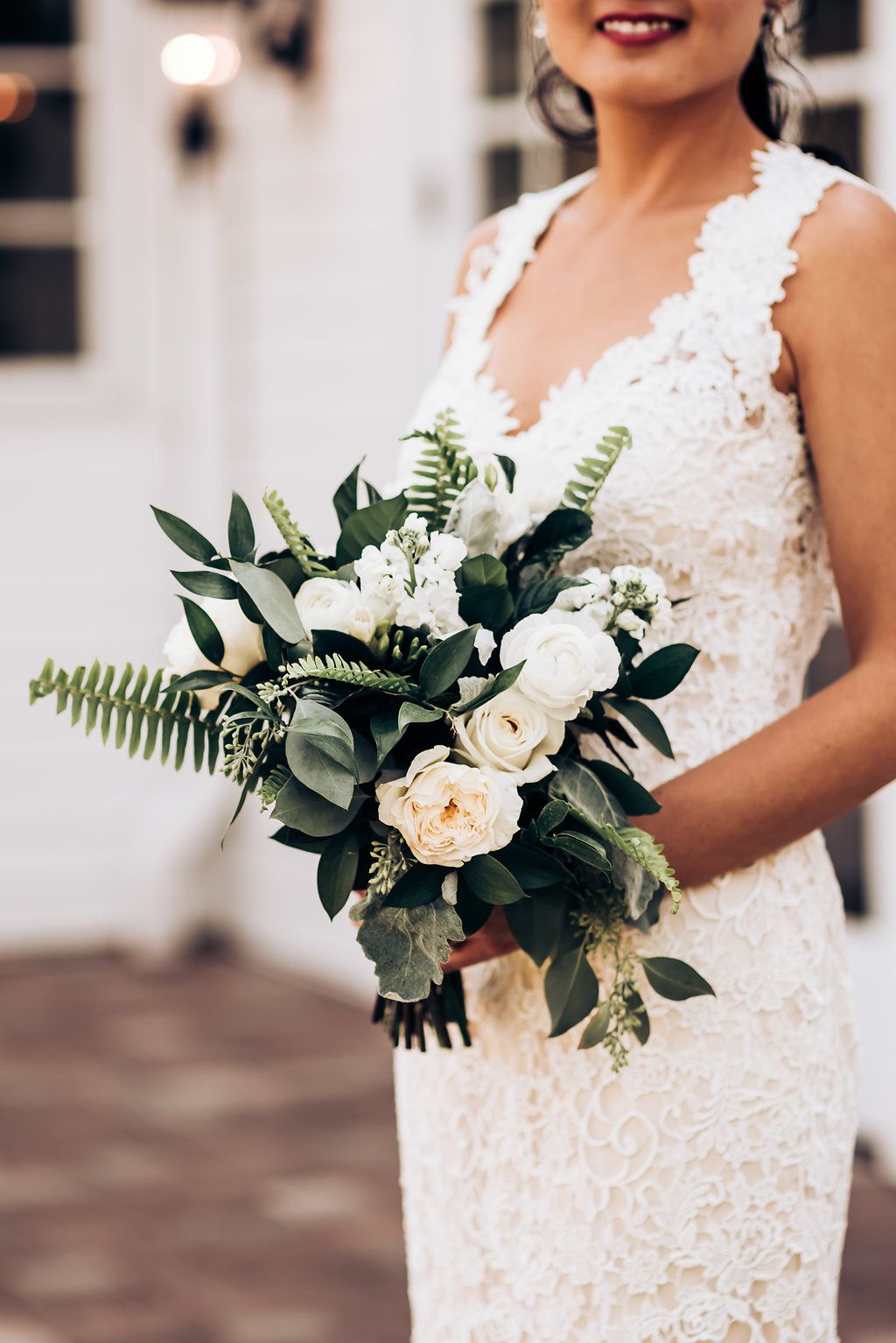 Close-up of white lace wedding dress and elegant green and white bouquet.