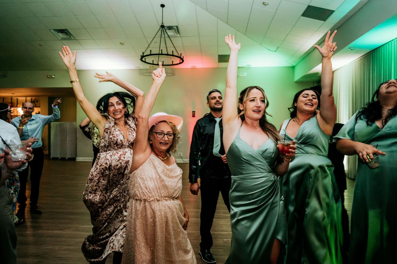 Wedding guests raising hands and celebrating on the dance floor at a reception.