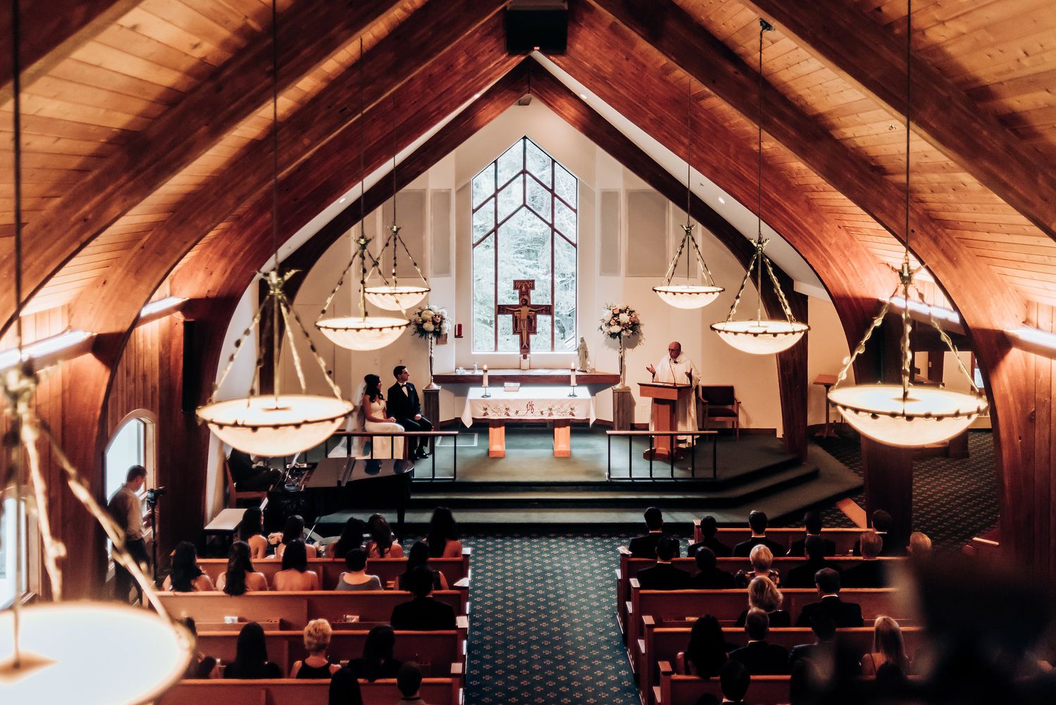 Church sanctuary with warm wood ceiling, hanging chandeliers and crucifix at front altar.