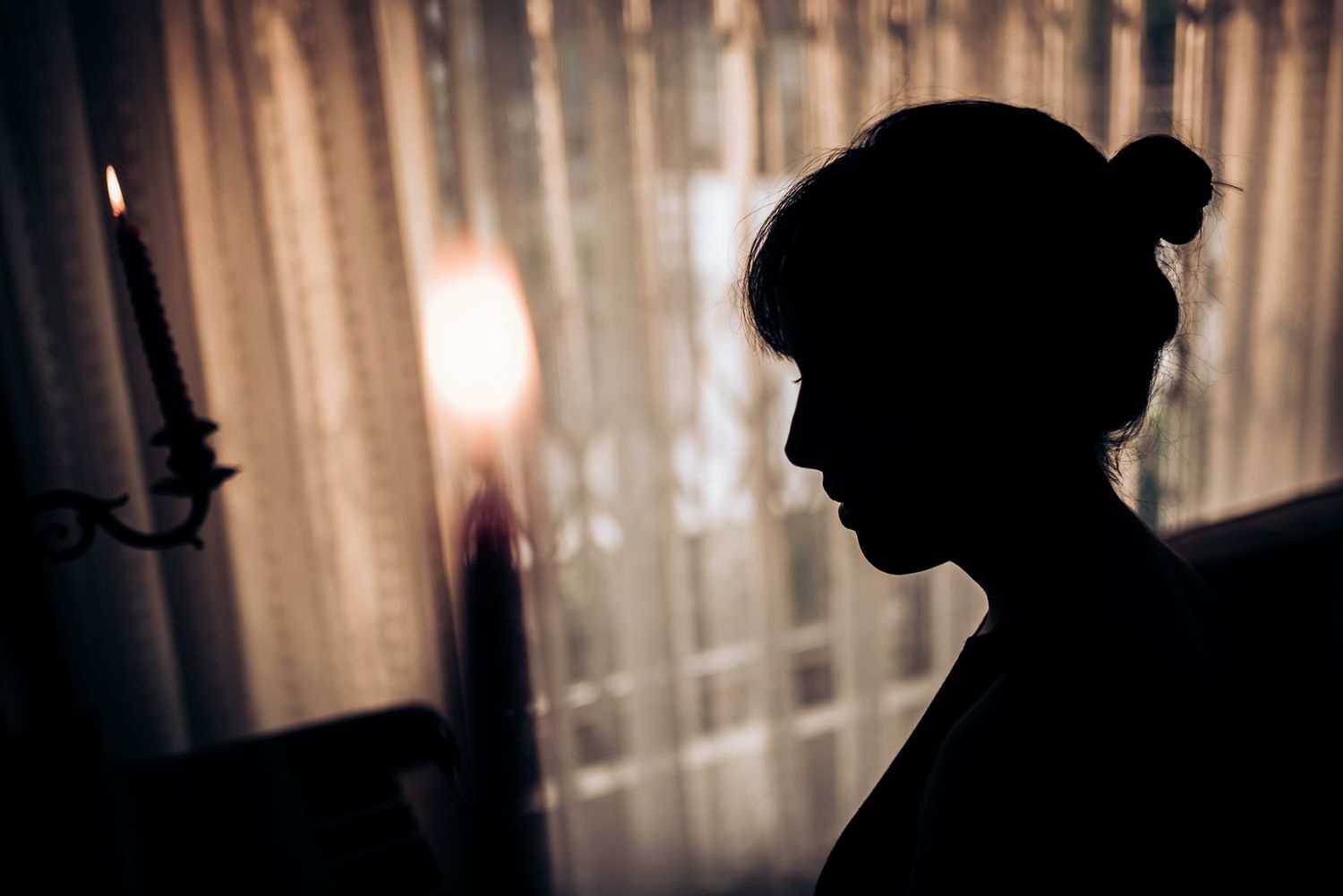 Silhouetted profile against sheer curtains in moody lighting.